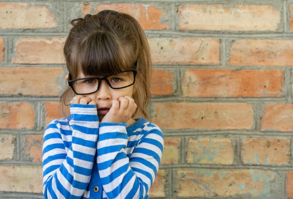 A little girl wearing glasses is covering her face with her hands.